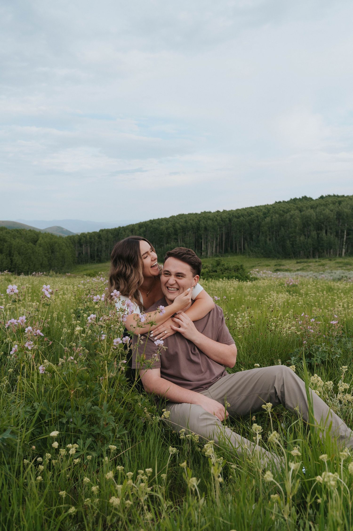A couple smiles as they take their engagements in a wildflower field near Park City Utah with their local photographer
