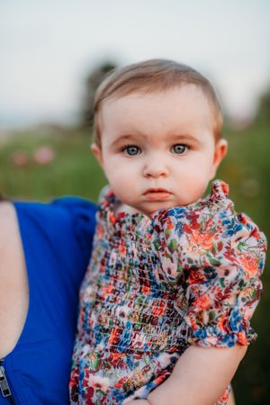 Baby wearing floral print outfit sitting outdoors in soft lighting.