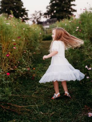 A whimsical twirl in a white dress among colorful garden flowers.