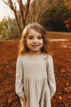 Fall portrait of young girl in beige dress standing on red autumn leaves.