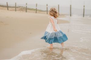 A joyful moment as a child in a tiered dress twirls and splashes in the ocean waves at the beach.