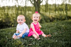 Two young children sitting together in grass with one wearing pink and one in white.