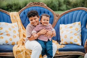 Two children sit together on an ornate blue vintage sofa with yellow pumpkin print pillows and blanket.