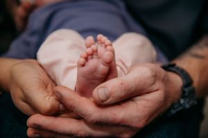 Close up of tiny newborn baby feet cradled in gentle hands.