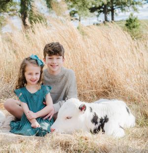 Family photo in golden grass field with white calf resting beside them.