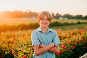 Young person posing in front of colorful wildflower field at golden sunset.