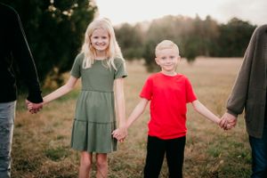 Children holding hands with parents walking in a field at sunset.