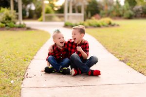 Two energetic children in matching plaid shirts laughing on garden pathway.