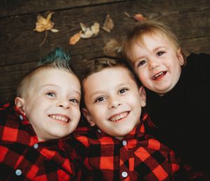 Three children in matching buffalo plaid shirts smiling at camera on rustic wood background.
