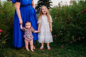 Two figures stand with someone in blue among wildflowers in a garden setting.