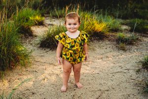 A cheerful summer outfit featuring a bright sunflower print romper against natural foliage.