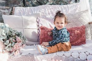 A cheerful moment captured on white bedding with decorative pillows and greenery in the background.