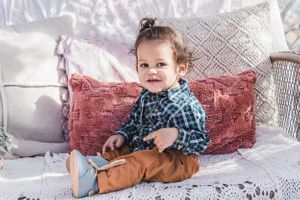 A child in plaid sitting on white bedding with decorative pillows.