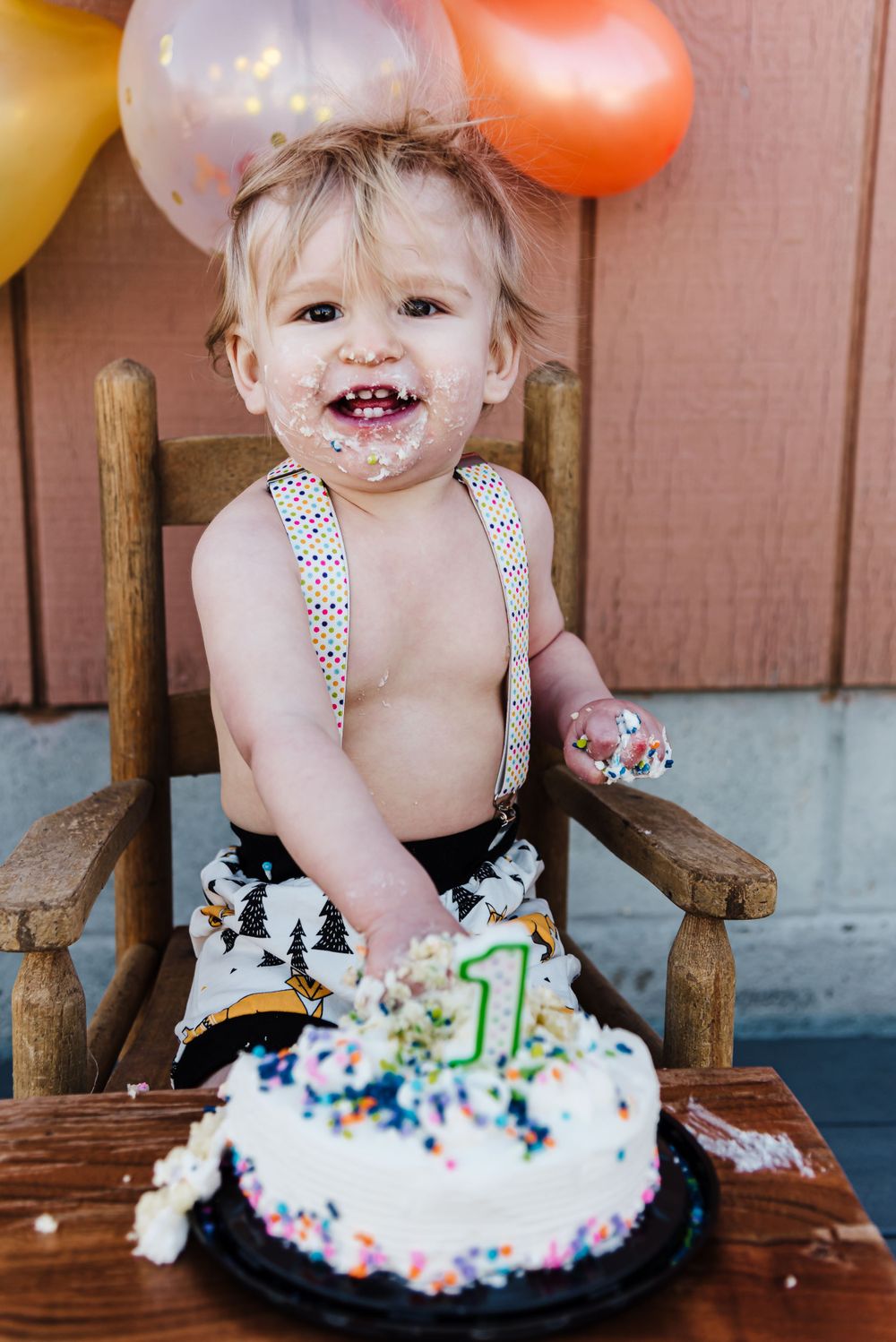 A first birthday celebration with cake covered in colorful sprinkles and festive balloons.