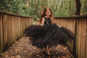 A dramatic black tulle dress twirling on a wooden walkway surrounded by autumn leaves.
