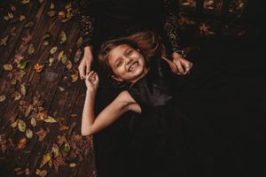 Joyful portrait of someone lying among autumn leaves in dark clothing.