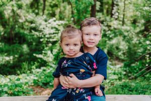 Two young children in navy outfits pose together outdoors in lush green setting.