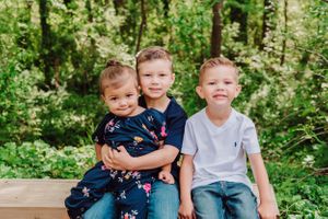 Three children sitting together on a wooden bench surrounded by greenery.