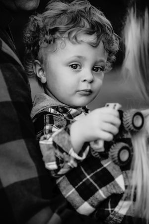 A black and white portrait of a young child wearing a plaid shirt while holding a toy camera.
