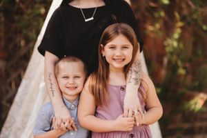 Sweet candid moment of three people posing together against wooden fence backdrop.