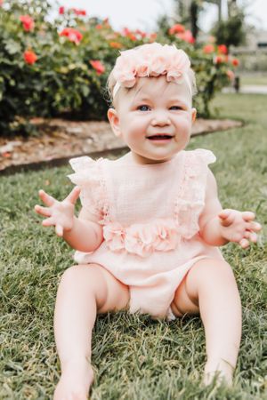 Baby in pink ruffled romper laughing during outdoor garden photoshoot.