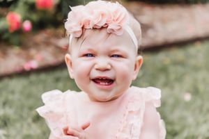 Baby wearing pink ruffled outfit smiling brightly in garden setting.
