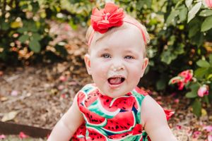 Joyful outdoor portrait of baby in watermelon print outfit near blooming roses.