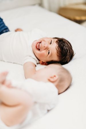 Joyful candid moment captured of children laughing while lying on white bedding.