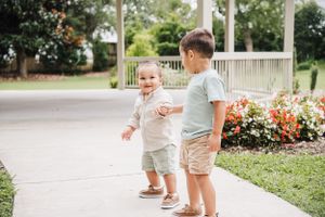 Two children interacting and smiling while standing on a path near flowering bushes.