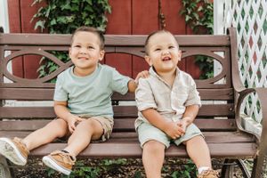 Two young children sitting and laughing together on a wooden bench outdoors.