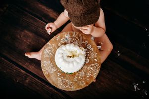 Overhead view of baby with white cake on decorative plate during cake smash photography.