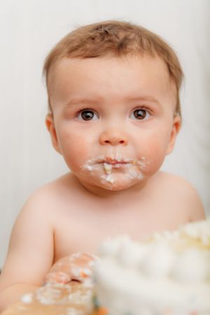 Close-up portrait of baby with cake frosting around mouth during smash cake session.