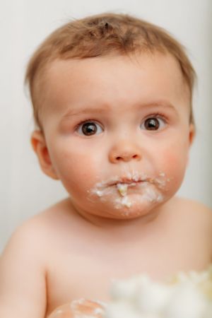 Portrait of baby covered in white cake frosting during first birthday photoshoot.