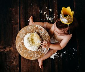 Overhead shot of baby wearing gold crown during cake smash session on wooden background.