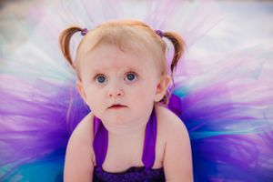 Child wearing purple tutu dress poses for portrait.