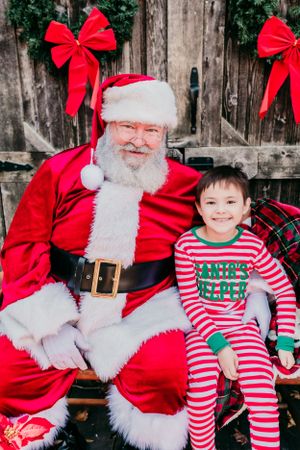 Festive portrait with Santa Claus and child in matching red and white striped holiday pajamas.