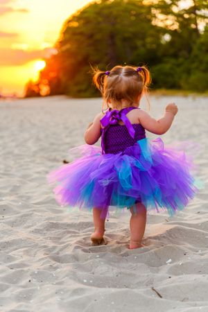 Toddler in purple and blue tutu dress dancing on beach at sunset.