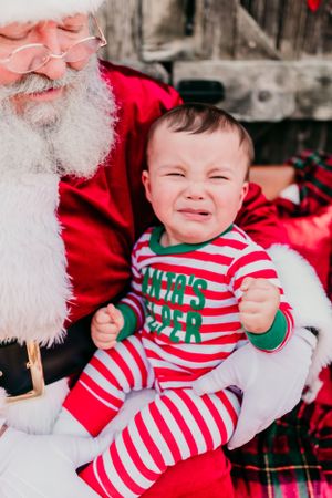 Holiday photo of baby in striped pajamas sitting with Santa Claus.
