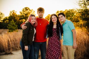 Group portrait of four people standing together in sunset-lit field wearing casual attire.