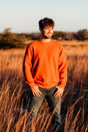 Person in bright orange sweater stands in golden field at sunset during outdoor portrait session.