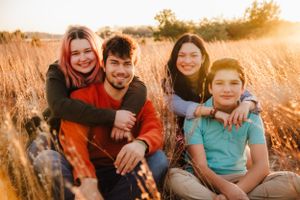 Family of four poses together in golden field during sunset photoshoot.