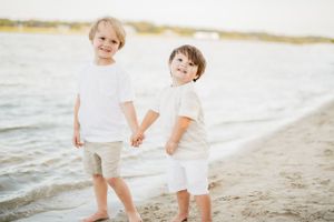 Two young children in white outfits holding hands while walking on a beach at sunset.