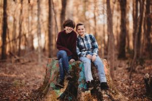 Two children sitting together on a tree stump in an autumn forest setting.
