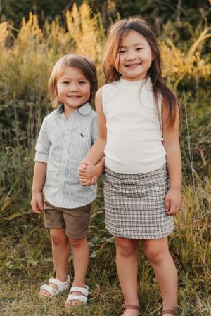 Two children in casual attire stand together against golden sunset grass backdrop.