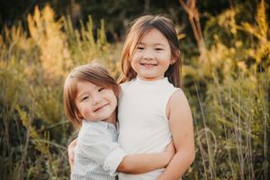 Two siblings embrace while smiling warmly at sunset in tall grass.