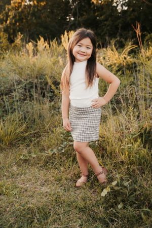 Child in white top and patterned skirt poses against sunset-lit field.