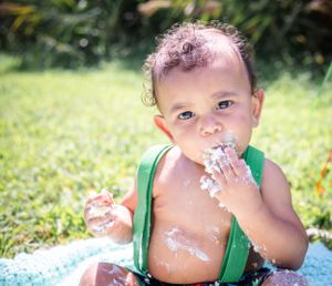 Toddler with cake frosting on face during outdoor smash cake photo session.