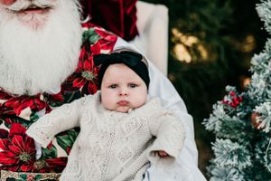 Baby in white sweater dress with Santa Claus during holiday photo session.