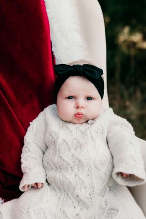 Close up of baby in white knit dress and black bow headband.