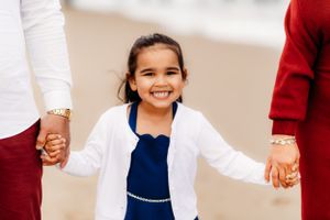 Smiling child in navy dress and white cardigan holding hands on sandy beach.